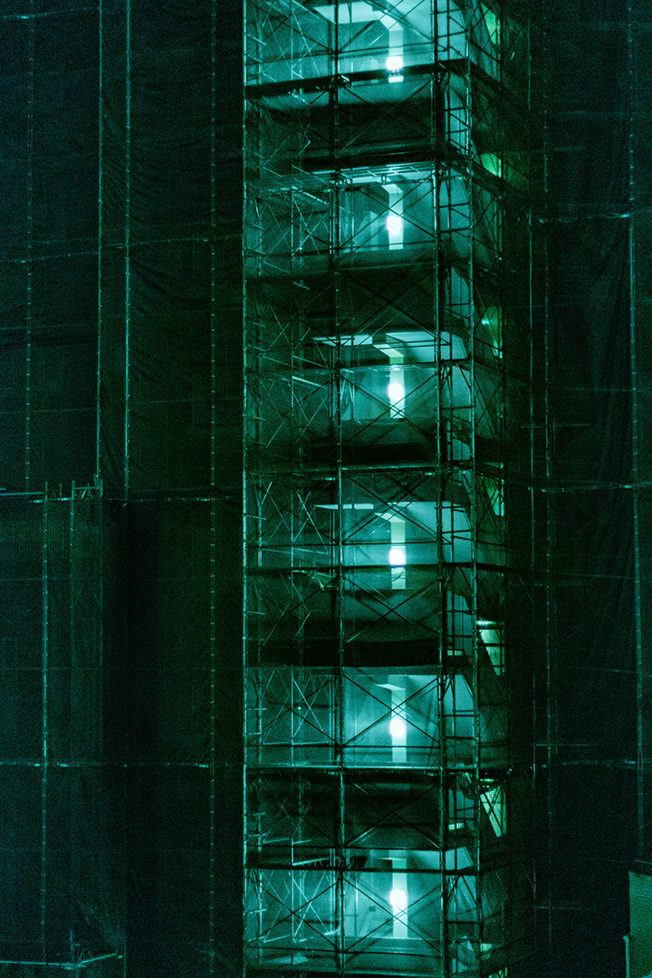 Construction scaffolding wrapped in a green net at night.